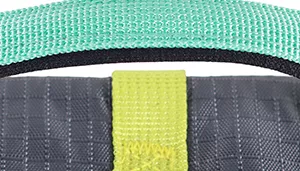 A swatch combining muted outdoor colors and rugged textures. The main panel is dark charcoal‑grey fabric with visible weave. A vertical seam of chartreuse‑yellow stitching runs centrally, bordered by dark gray material. The materials appear durable and textured, evoking an outdoor‑gear aesthetic.